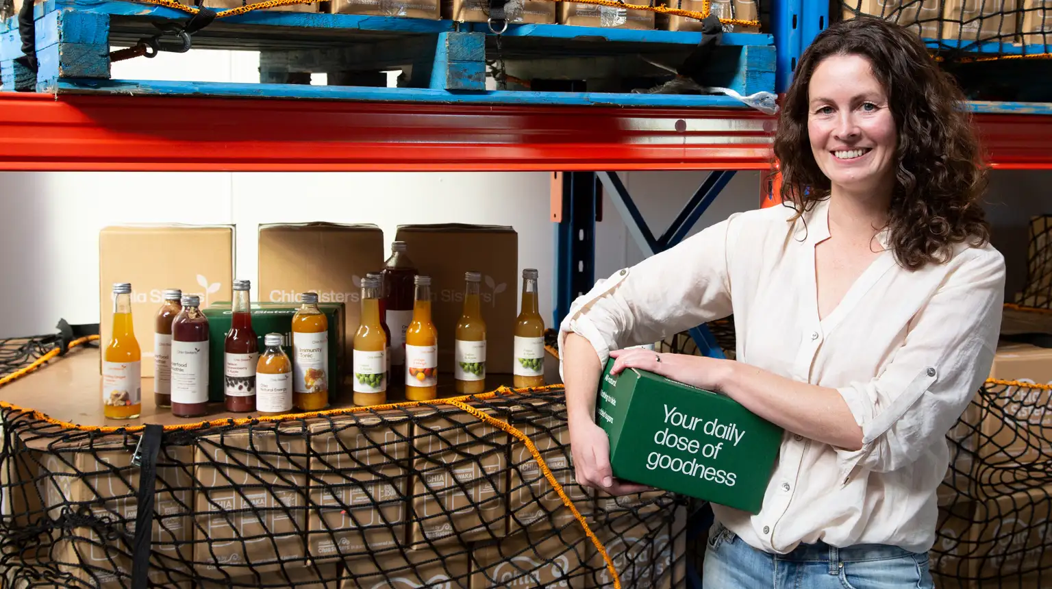 A person holding a green box beside a display of bottled drinks in a warehouse.