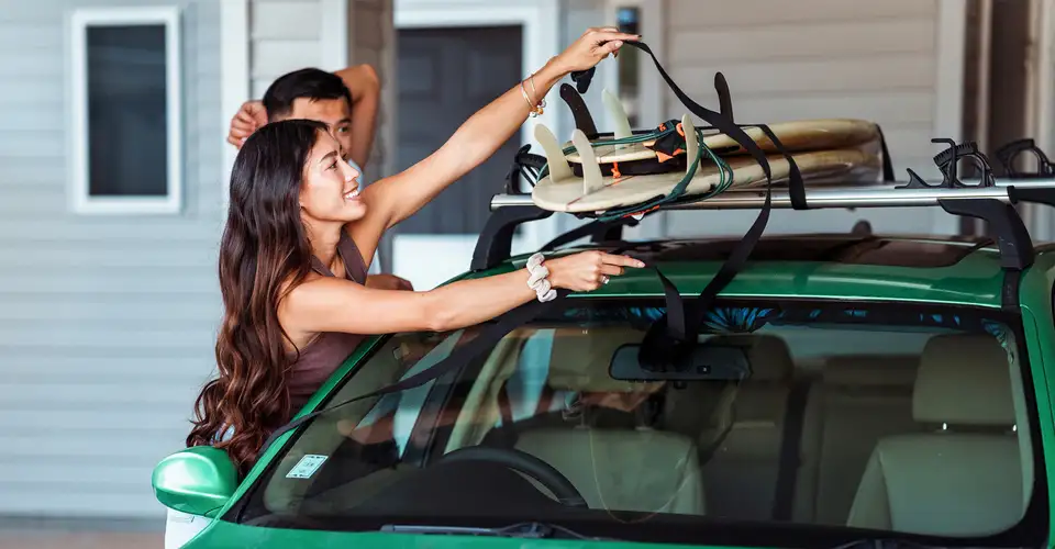 People securing surfboards to car roof rack outside house