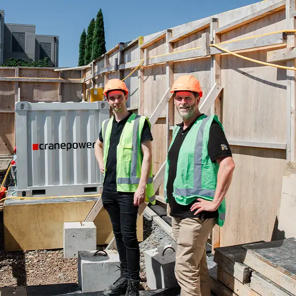 Two people in safety gear standing at a construction site beside a Cranepower unit.