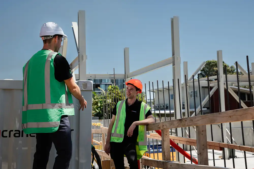 Two workers in safety gear talking at a construction site beside a Cranepower unit.