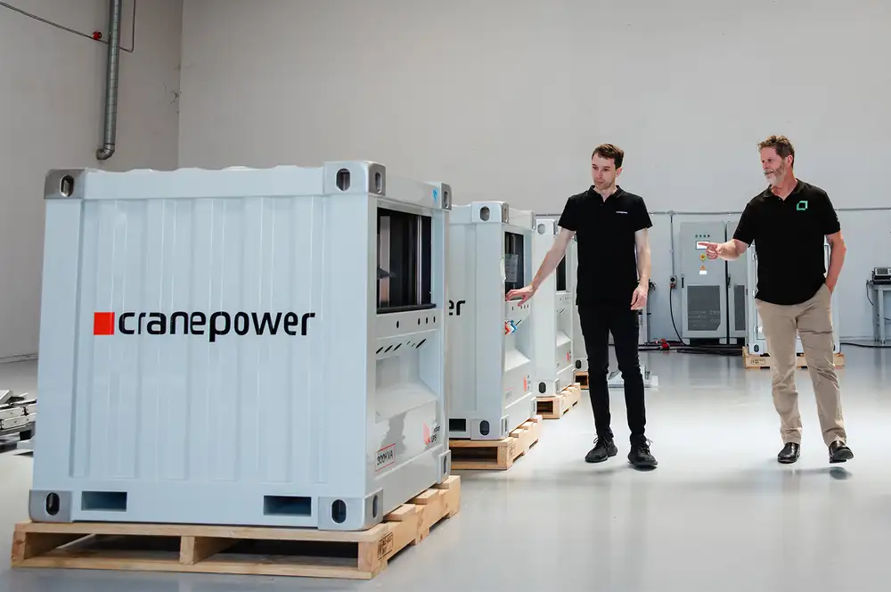 Two people standing beside Cranepower units inside a bright industrial studio.