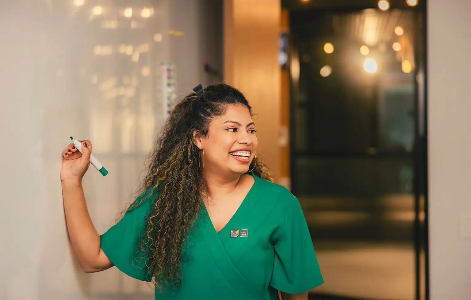 Person in a green top writing on a whiteboard in an office setting.