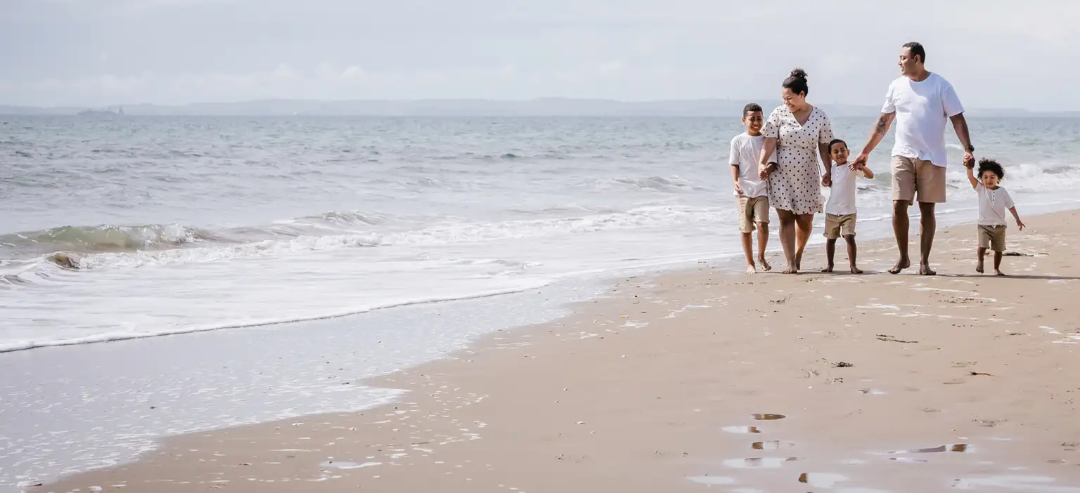 Group of people walk along sandy beach beside ocean shoreline wide shot