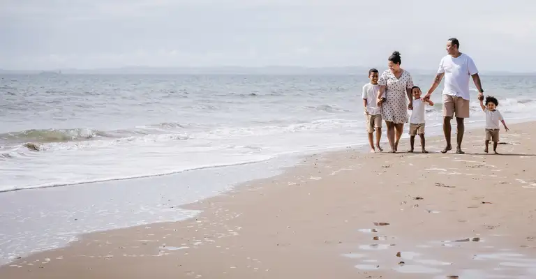 Group of people walk along sandy beach beside ocean shoreline wide shot