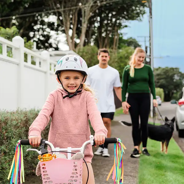 Child riding bike suburban street adults walking dog background