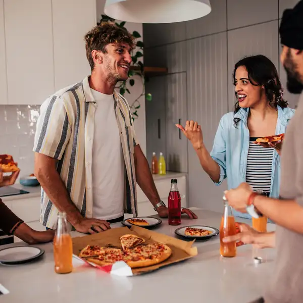Group sharing pizza around kitchen bench at home