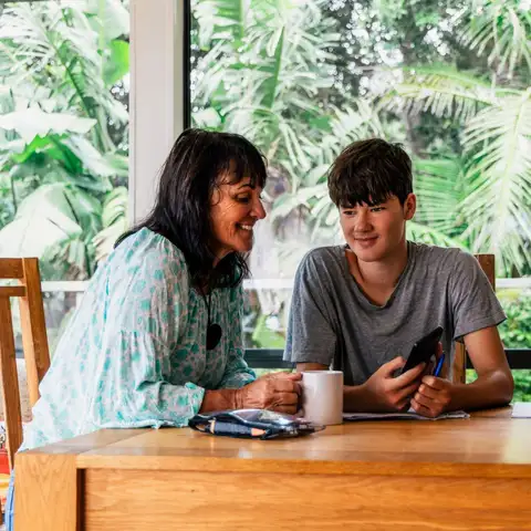 Adult and child study together at dining table with notebooks and phone