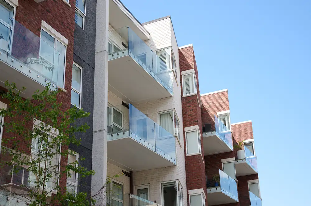 Modern apartment building with brick and white cladding and glass‑balconied units against a blue sky.