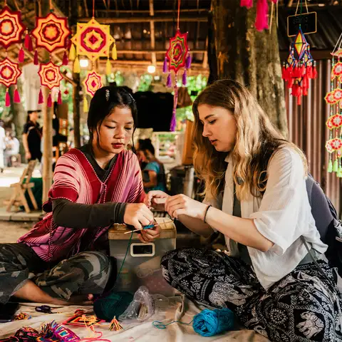 Two people make crafts at market stall with hanging decorations