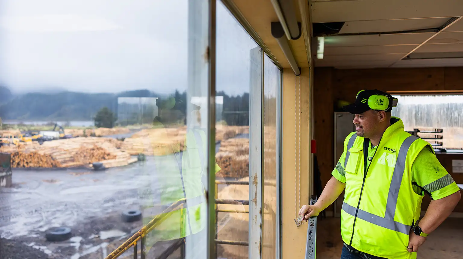 Man in hi-vis at a window looking over a timber yard.