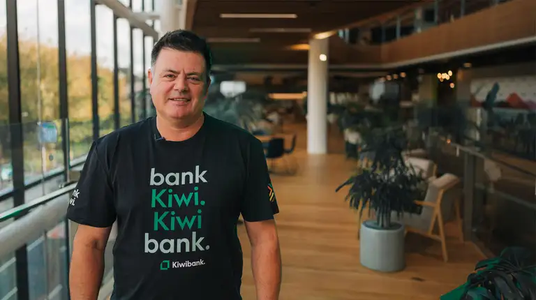 Kiwibank CEO standing in office wearing "bank Kiwi. Kiwibank." t-shirt