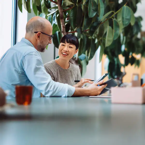 Two professionals, a man and a woman, having a discussion in a leafy office.