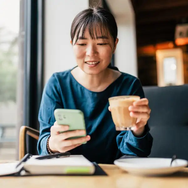 Person checking phone while holding coffee in café