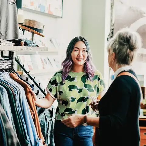 Two women talking and browsing clothes in a bright, welcoming shop.