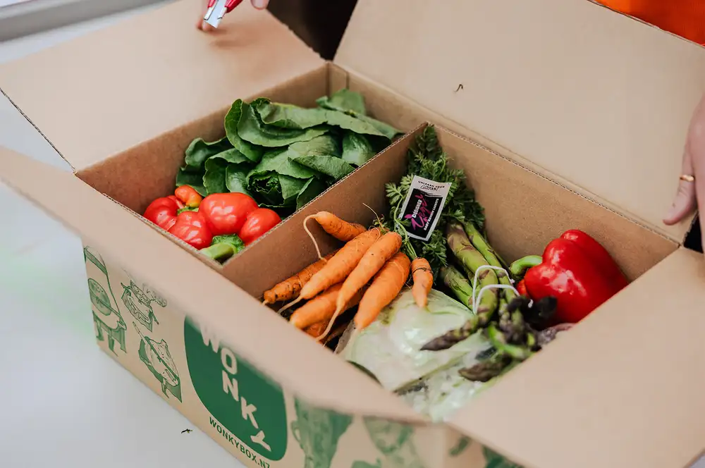 An open box filled with fresh vegetables, including carrots, capsicum, greens and asparagus.