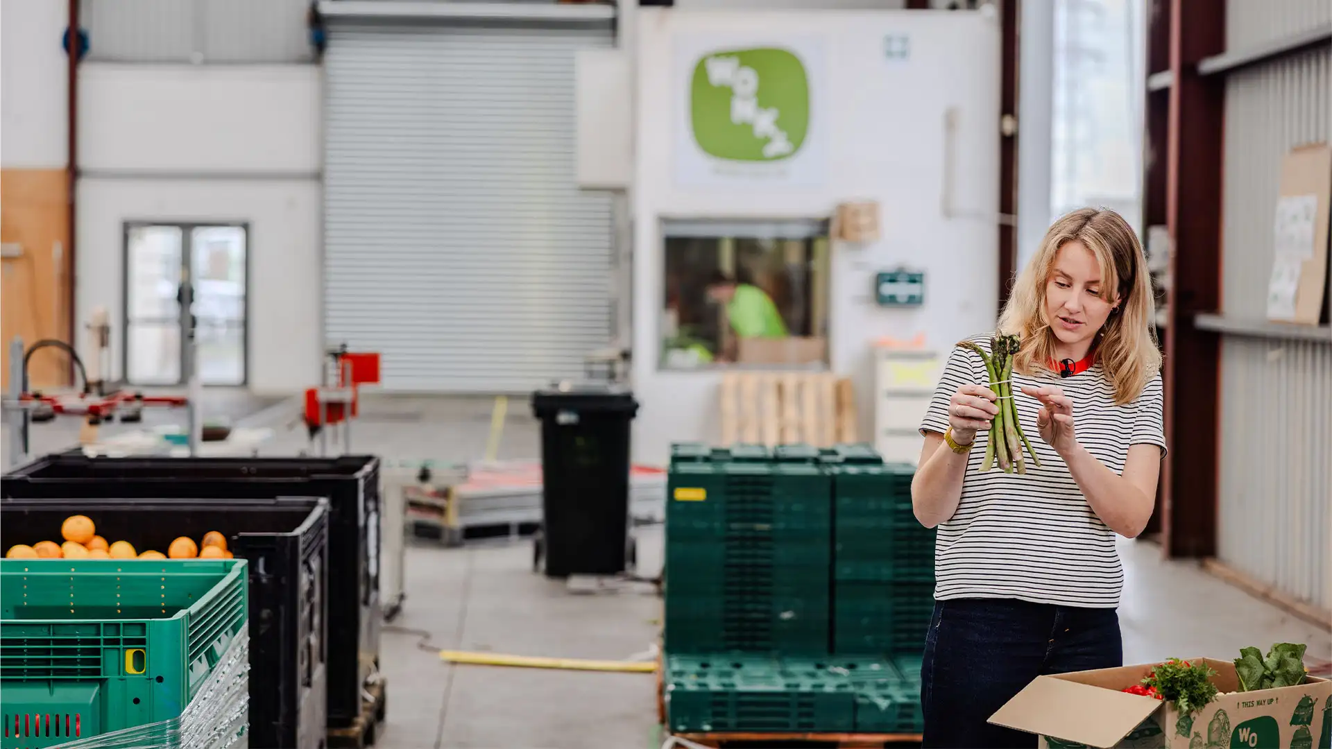 A person sorting fresh produce inside a warehouse with crates of fruit and vegetables.